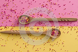 Sugar sprinkle dots In a wooden spoon on pink and yellow background,decoration for cake and bakery