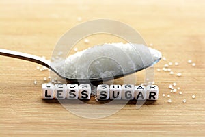 Less sugar text from tiled letter blocks and sugar pile on a spoon suggesting dieting concept