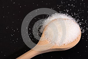 Sugar in wooden spoon on black background