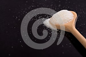 Sugar in wooden spoon on black background