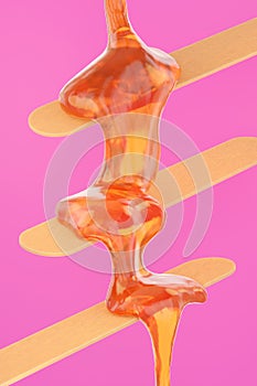 Sugaring paste flows on wooden sticks for hair removal procedure.