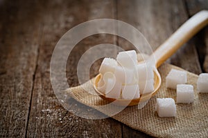 Sugars cube in wooden spoon on jute napkin over wooden background