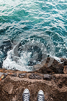 Suicidal ideation or thoughts, young person standing at the ocean cliff above the cold water and sea foam after waves crashing at