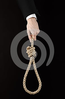 Suicide and business topic: Hand of a businessman in a black jacket holding a loop of rope for hanging on black isolated