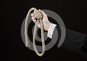 Suicide and business topic: Hand of a businessman in a black jacket holding a loop of rope for hanging on black isolated