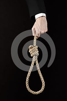 Suicide and business topic: Hand of a businessman in a black jacket holding a loop of rope for hanging on black isolated