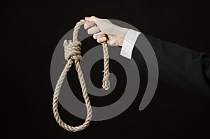 Suicide and business topic: Hand of a businessman in a black jacket holding a loop of rope for hanging on black isolated