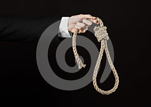 Suicide and business topic: Hand of a businessman in a black jacket holding a loop of rope for hanging on black isolated