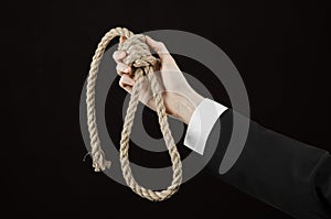 Suicide and business topic: Hand of a businessman in a black jacket holding a loop of rope for hanging on black isolated