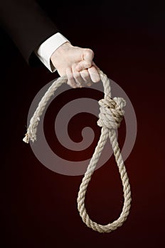 Suicide and business topic: Hand of a businessman in a black jacket holding a loop of rope for hanging on dark red isolated