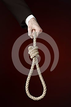 Suicide and business topic: Hand of a businessman in a black jacket holding a loop of rope for hanging on dark red isolated