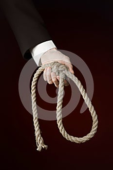 Suicide and business topic: Hand of a businessman in a black jacket holding a loop of rope for hanging on dark red isolated