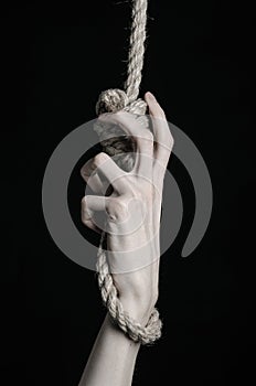 Suicide and depression topic: human hand hanging on rope loop on a black background