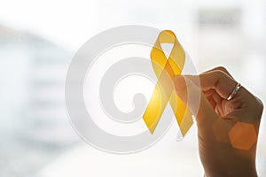 Suicide prevention and Childhood Cancer Awareness, Yellow Ribbon on wooden background  for supporting people living and illness.