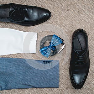 Suit, blue bow tie, leather black shoes and belt. Grooms wedding morning. Close up of modern man accessories