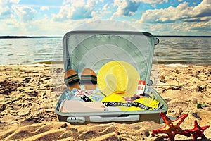 Suitcase with clothes and different things for trip lying closeup on the sand beach in summertime