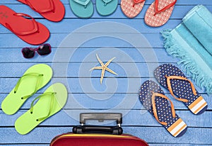 Suitcase with flip-flops, beach towel and sunglasses on wooden table.