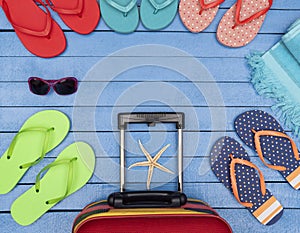 Suitcase with flip-flops, beach towel and sunglasses on wooden table.