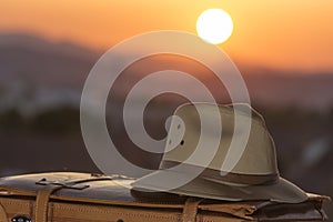 Suitcase and hat at sunset, allusion to travel, beginning of vacation