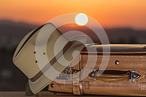 Suitcase and hat at sunset, allusion to travel, beginning of vacation