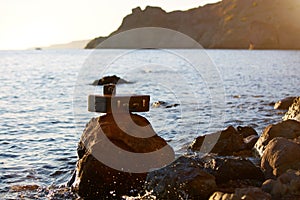 Suitcase with photocamera on stone. Nature view. Travel desire. Beach vacation. Summer time. Adventure trip and seaview