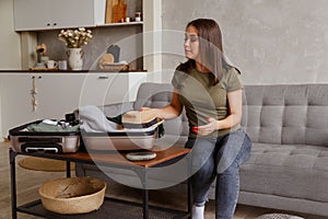 Suitcase preparation for a vacation trip after lock down. Young woman checking clothes and stuff in luggage on the sofa