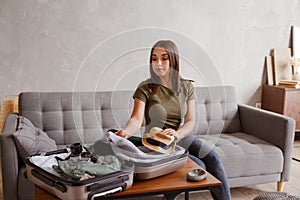 Suitcase preparation for a vacation trip after lock down. Young woman checking clothes and stuff in luggage on the sofa