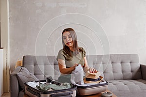 Suitcase preparation for a vacation trip after lock down. Young woman checking clothes and stuff in luggage on the sofa