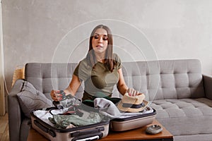 Suitcase preparation for a vacation trip after lock down. Young woman checking clothes and stuff in luggage on the sofa