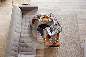 Suitcase preparation for a vacation trip. Young woman checking clothes and stuff in luggage on the sofa. View from above