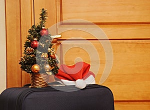 Suitcase and santa hat against a wooden door.