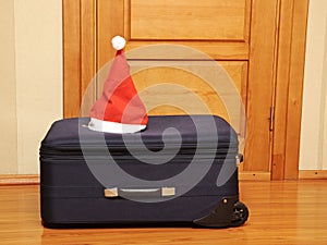 Suitcase and santa hat against a wooden door.