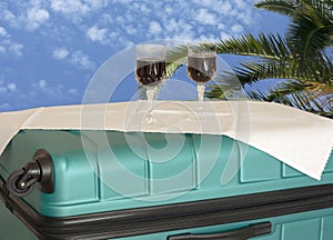 Suitcase staycation and wine for two set as table. Distant blue skies and palm tree for dreams of a future vacation.