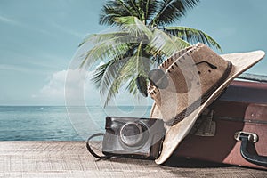 Suitcase, sun hat, photo camera and sunglasses with sea water, coconut palm tree and blue sky background on sunny summer day in