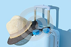 Suitcase with sunglasses and hat on a pastel blue background. Travel concept