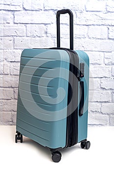 suitcase on wheels stands against a brick wall