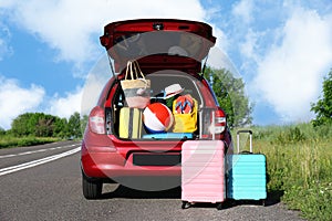 Suitcases near family car with open trunk full of luggage