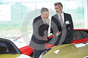 Suited car salesman in luxury forecourt photo