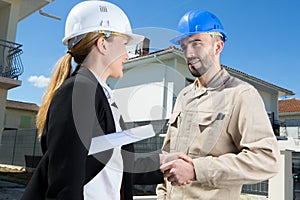 Suited woman shaking hands with workman by residential property