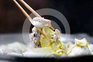 Sukiyaki soup served in the ceramic bowl with speical sauce. Chopsticks tongs with vegetable and pork