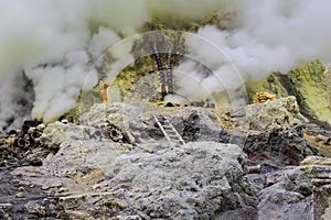 Sulfur mining operation, Mount Ijen volcano crater, Indonesia.Volcanic gas rising from ground. Yellow sulfur scattered on ground
