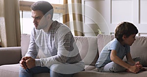 Sullen father and child son sit on sofa avoiding talk