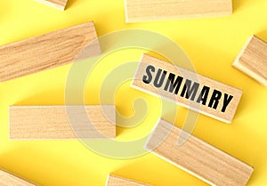 SUMMARY text written on a wooden blocks on a yellow background.