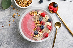 Summer acai smoothie bowls with raspberries, banana, blueberries, and granola on gray concrete background. Breakfast bowl with