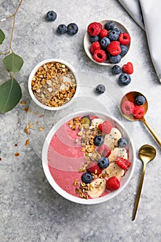 Summer acai smoothie bowls with raspberries, banana, blueberries, and granola on gray concrete background. Breakfast bowl with