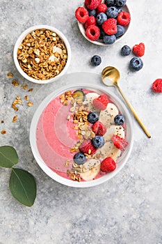 Summer acai smoothie bowls with raspberries, banana, blueberries, and granola on gray concrete background. Breakfast bowl with