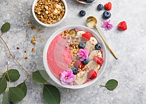 Summer acai smoothie bowls with raspberries, banana, blueberries, and granola on gray concrete background. Breakfast bowl with