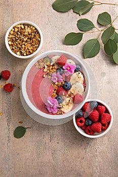 Summer acai smoothie bowls with raspberries, banana, blueberries, and granola on gray concrete background. Breakfast bowl with