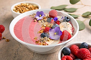 Summer acai smoothie bowls with raspberries, banana, blueberries, and granola on gray concrete background. Breakfast bowl with