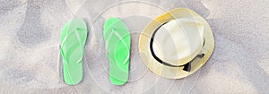 Summer accessories on beach texture banner background. Green Flip flops and hat on sand top view. Slippers shoes and vacation